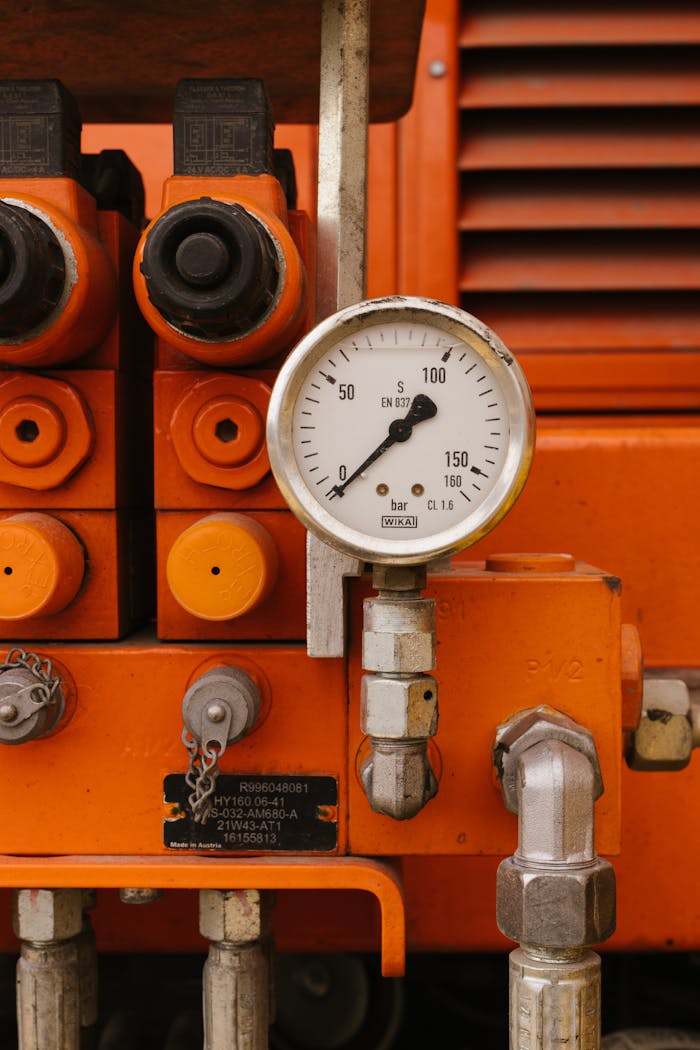 Detailed view of a pressure gauge on orange industrial machinery, showcasing engineering equipment.